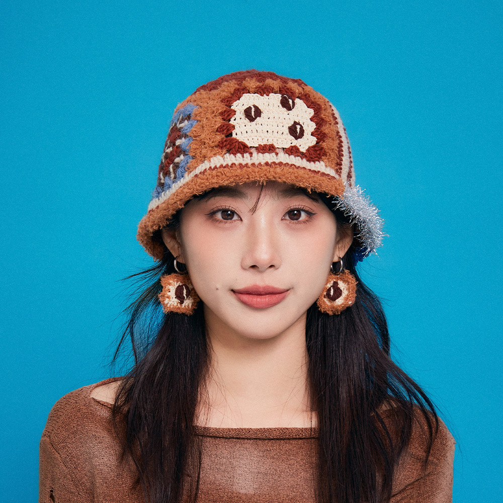 Front view of a model wearing the Refreshing Coffee Crochet Bucket Hat, highlighting the brown tones and a white granny square patch with stitched coffee bean motifs.
