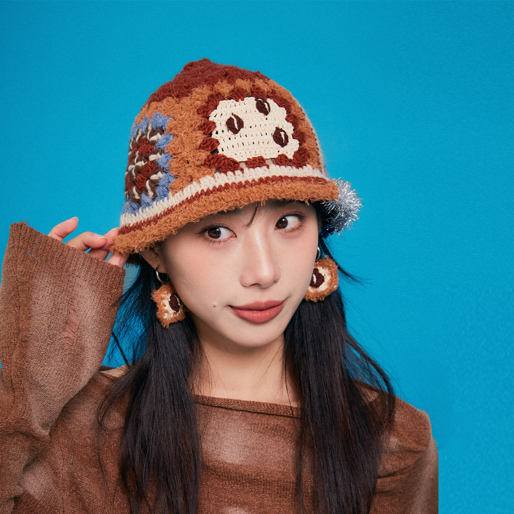 Lifestyle shot of a model wearing the Refreshing Coffee Crochet Bucket Hat against a vibrant blue background, showcasing a stylish winter street fashion look.