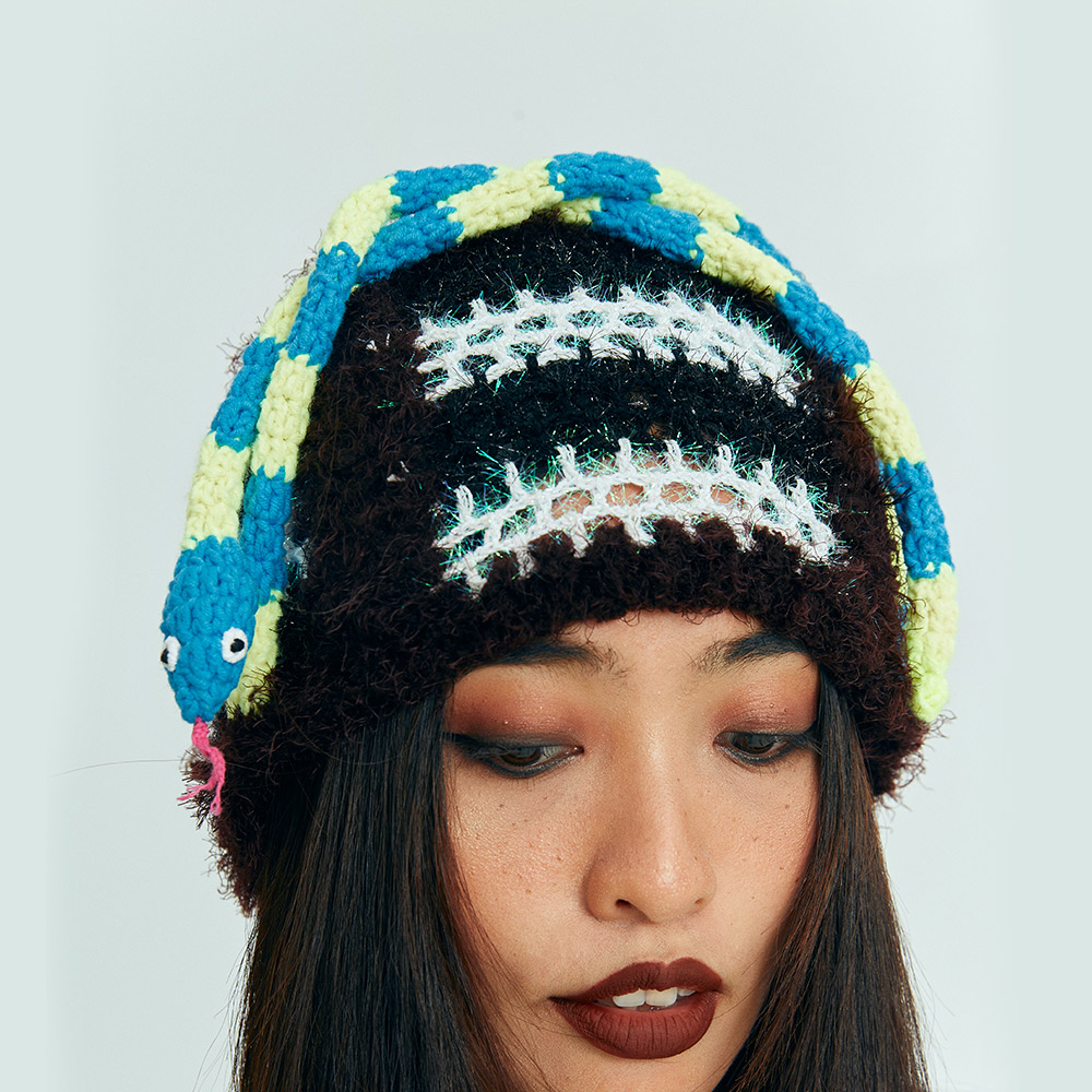 Close-up of a model featuring the Snake Crochet Hat with its long blue and yellow striped braids wrapped playfully over the top.