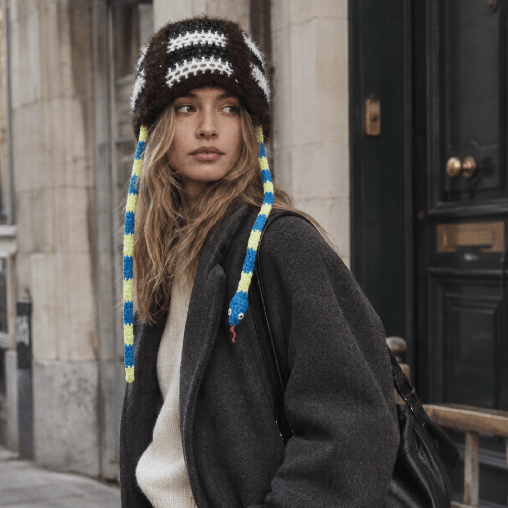 FeekyStore architectural snake hat with blue and yellow patterned ties, styled with a dark wool coat in a European city street setting.