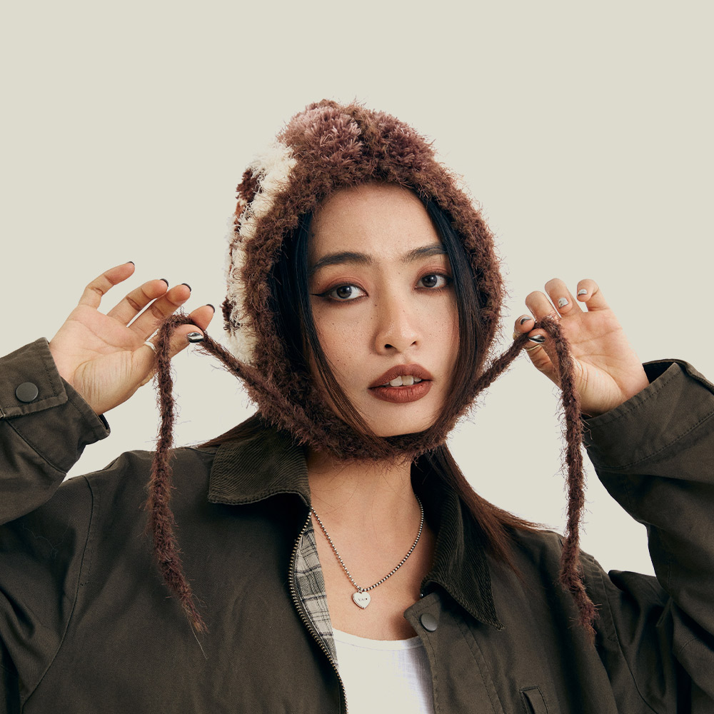 Front view of a model wearing the Vintage Grid Crochet Hat, featuring cozy earflaps and long dangling chin ties.