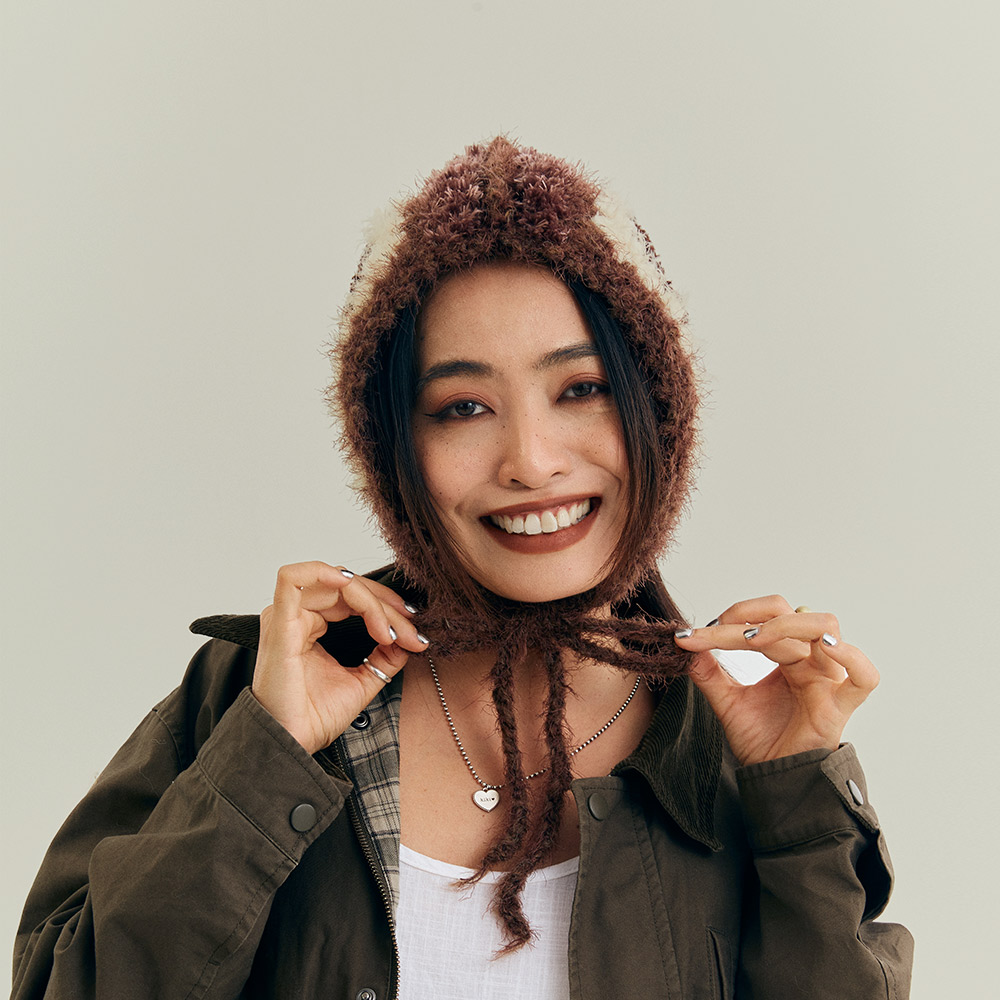 Smiling front view of a model styling the vintage grid crochet hood hat, tied loosely for a casual, warm winter look.