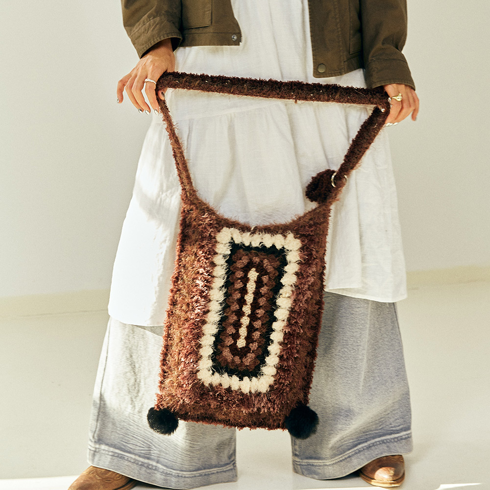 A model holding the long strap of the Vintage Grid Crochet Tote Bag downwards, illustrating the clean rectangular shape and premium artisan stitch loops.