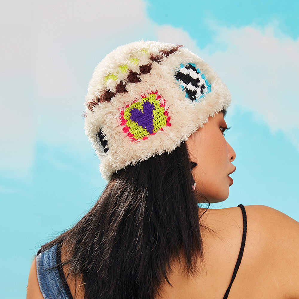 An angled back view of the Warm Cow Velvet Crochet Hat on a model, displaying a bold purple and green heart pattern on the textured yarn.