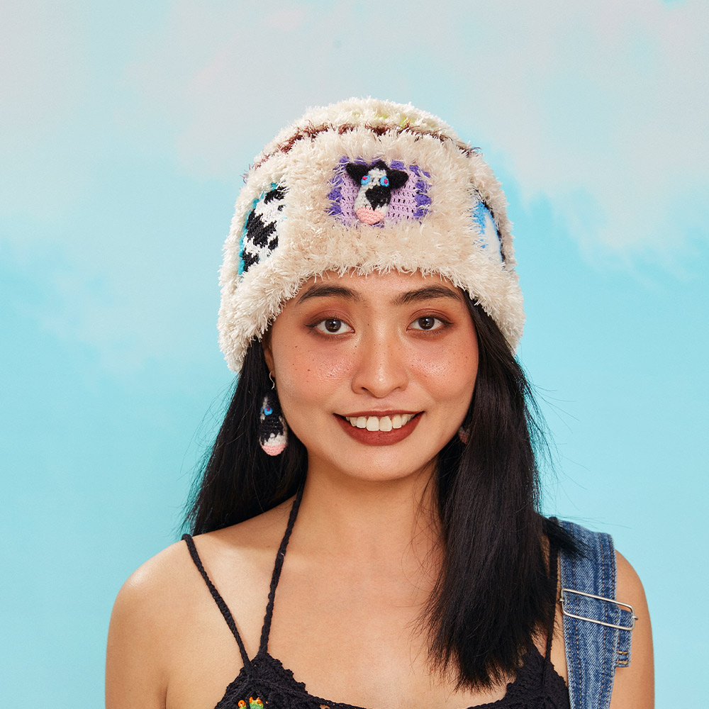 Front view of a model wearing the Warm Cow Velvet Crochet Hat, showcasing the fuzzy velvet texture and a classic black and white cow print granny square patch.