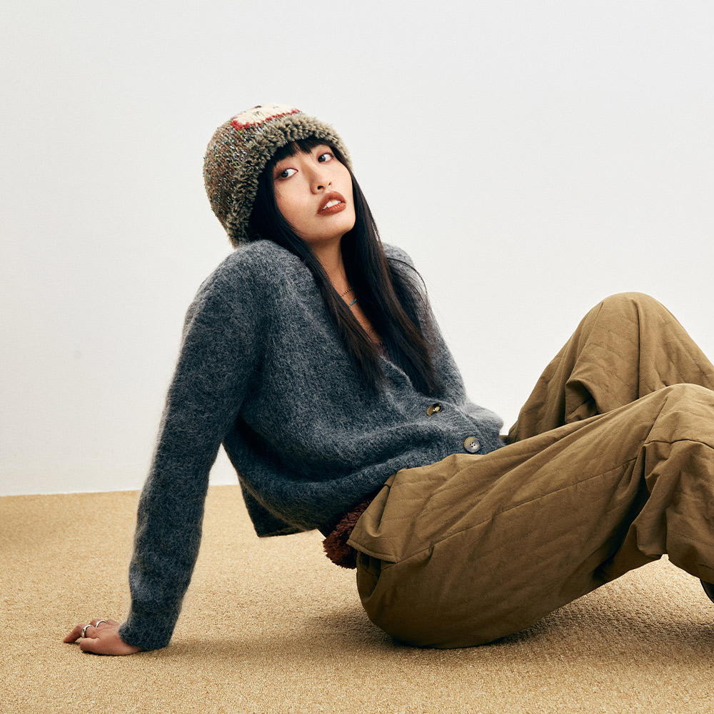 Full-body look of a model lounging on the floor, styling the Wool Apple Crochet beanie with a cozy grey winter sweater.