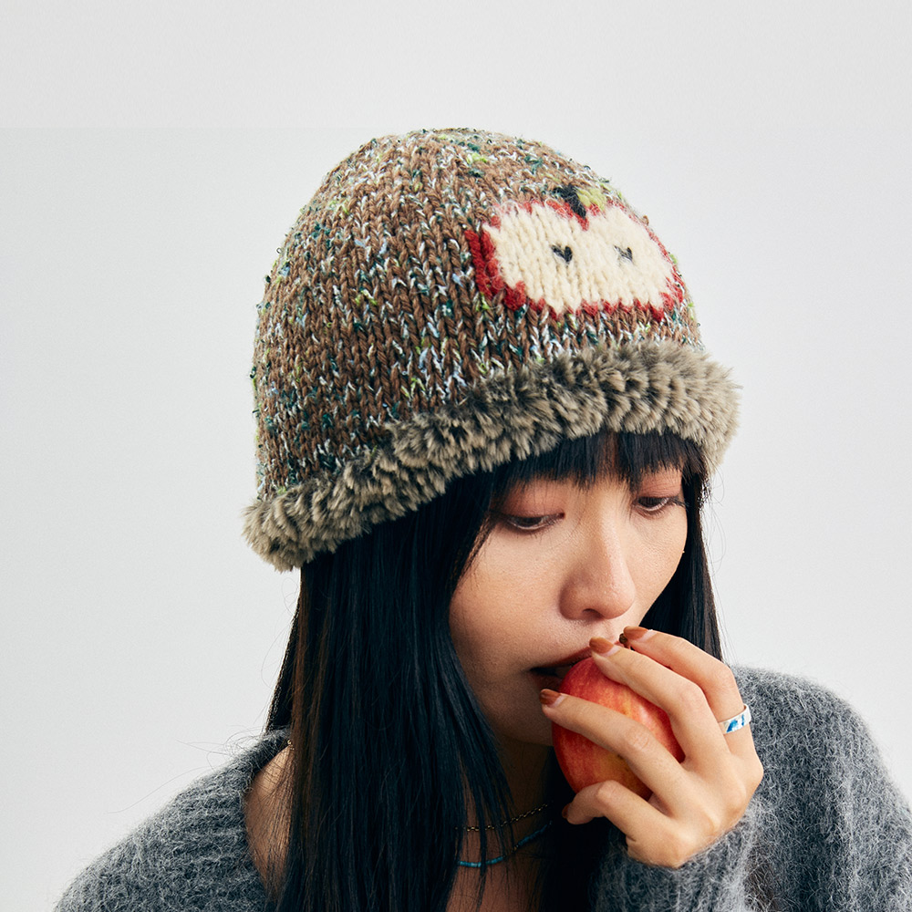 Lifestyle shot of a model wearing the Wool Apple Crochet beanie while holding an apple, presenting a cozy and playful aesthetic.