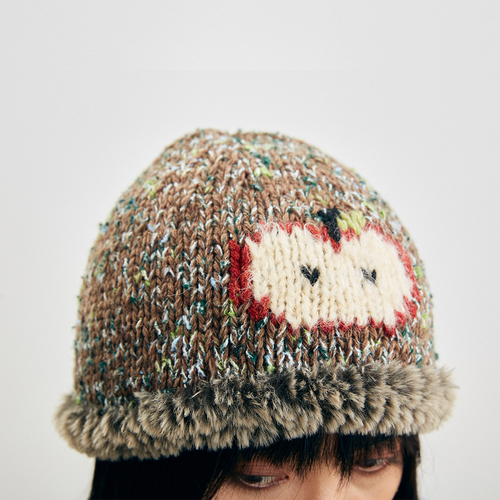 Close-up front view of the Wool Apple Crochet Hat on a model, showcasing the detailed red and white apple pattern and the fuzzy textured brim.