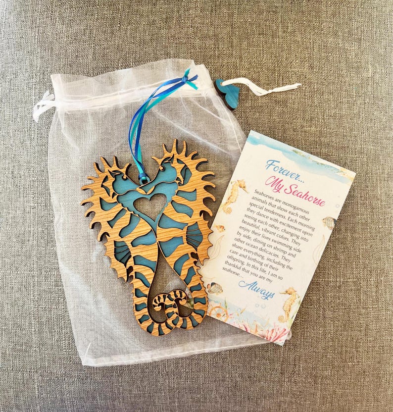 可能包含:一个蓝棕色木质海马摆件。两只海马交织成心形。摆件附带一张小卡片,上面写着“永远……我的海马”,并附有海马的介绍。