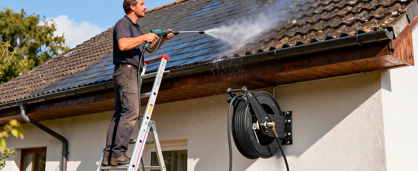 Man standing on a ladder cleaning a roof with a BreAro pressure washer connected to a wall-mounted retractable hose reel, spraying water on roof tiles outdoors.