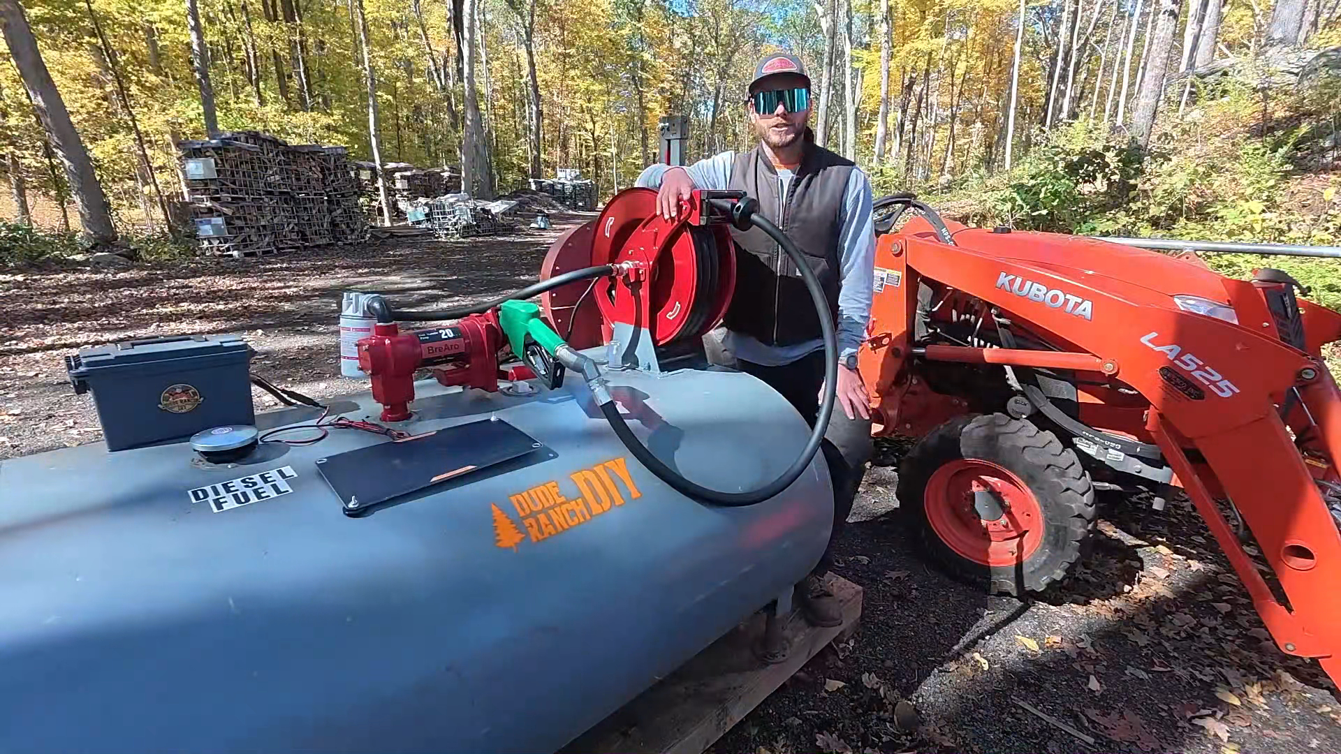 BreAro fuel hose reel and transfer pump setup on a diesel fuel tank, used for refueling a Kubota tractor in an outdoor farm setting.