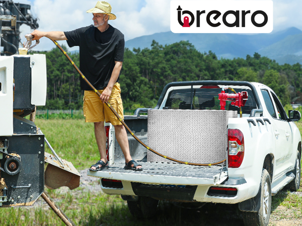 Man refueling equipment using a BreAro 20 GPM fuel transfer pump installed on a truck bed, set in a green field with mountains in the background, showcasing reliable and efficient fuel transfer.