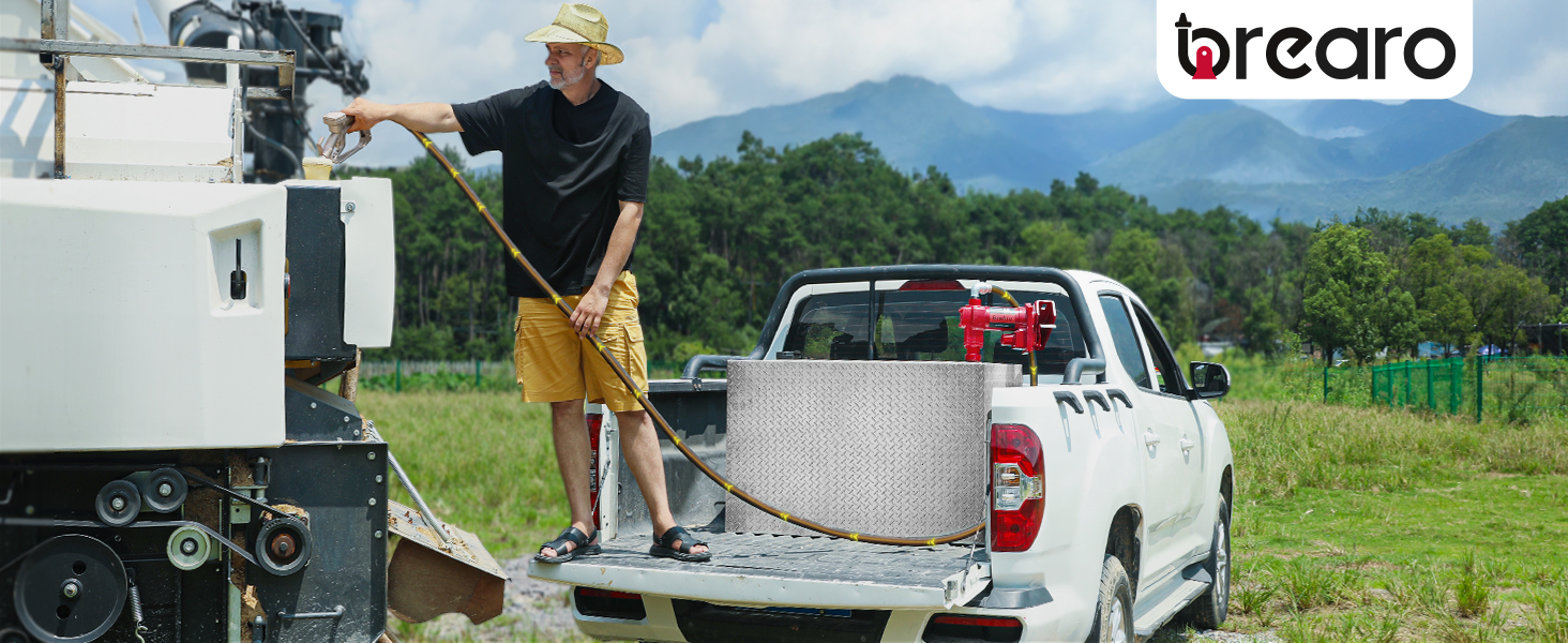 Man refueling equipment using a BreAro 20 GPM fuel transfer pump installed on a truck bed, set in a green field with mountains in the background, showcasing reliable and efficient fuel transfer.