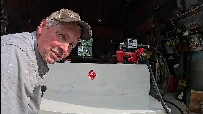 Man demonstrating a Brearo fuel transfer pump setup in a workshop, showing tank connection and GPM meter in use.