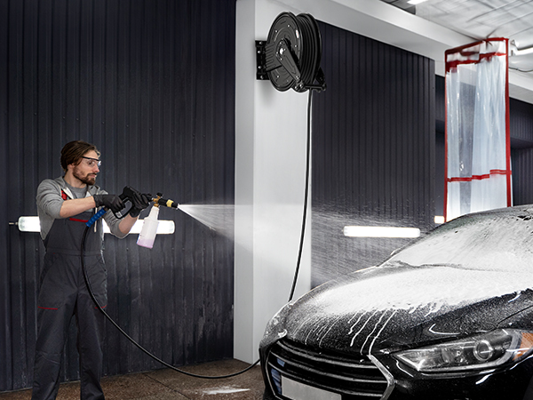 BreAro retractable hose reel in use during a car wash. Wall-mounted for convenience, it provides smooth operation and efficient cleaning, ideal for professional automotive detailing and maintenance tasks.