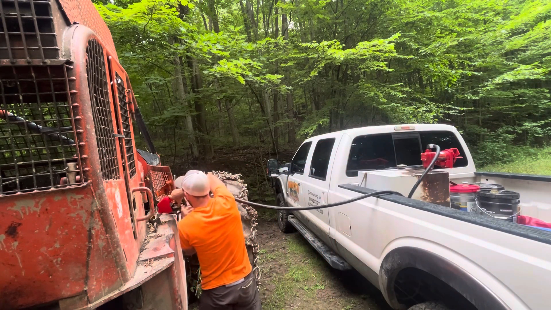 A construction worker fueling heavy machinery with a high-flow diesel fuel transfer pump at a remote job site in the forest.