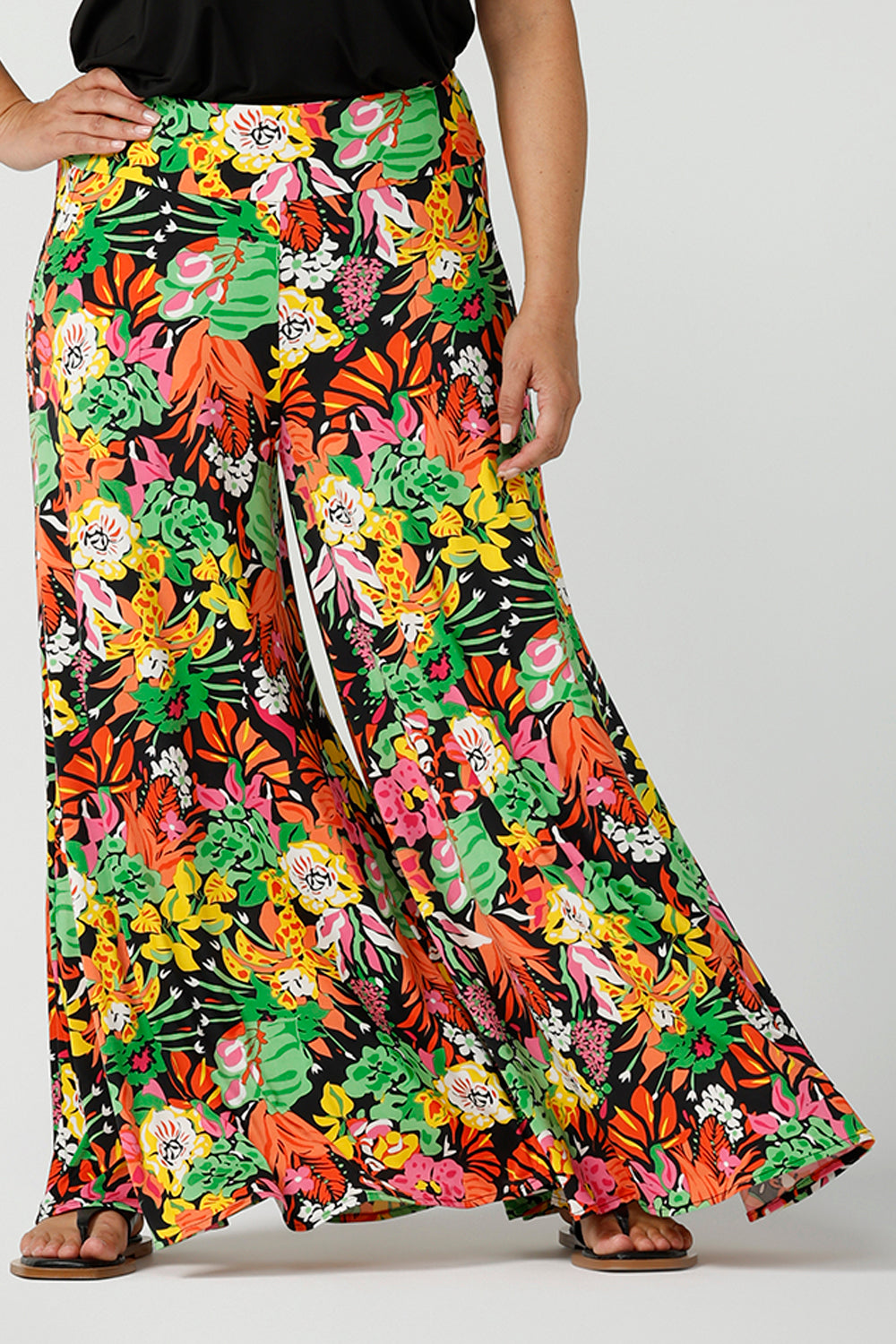 Close up of a size 12 woman wearing the Caspian Palazzo pant n a beautiful bright colourful print. In soft and lightweight jersey this pant features side pocket and a wide leg opening. Styled back with a black cami top and flat sandals. A perfect look for