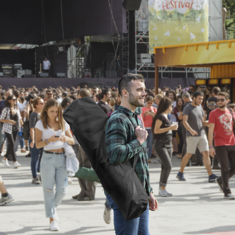 Man carrying chair storage bag walking through festival. 