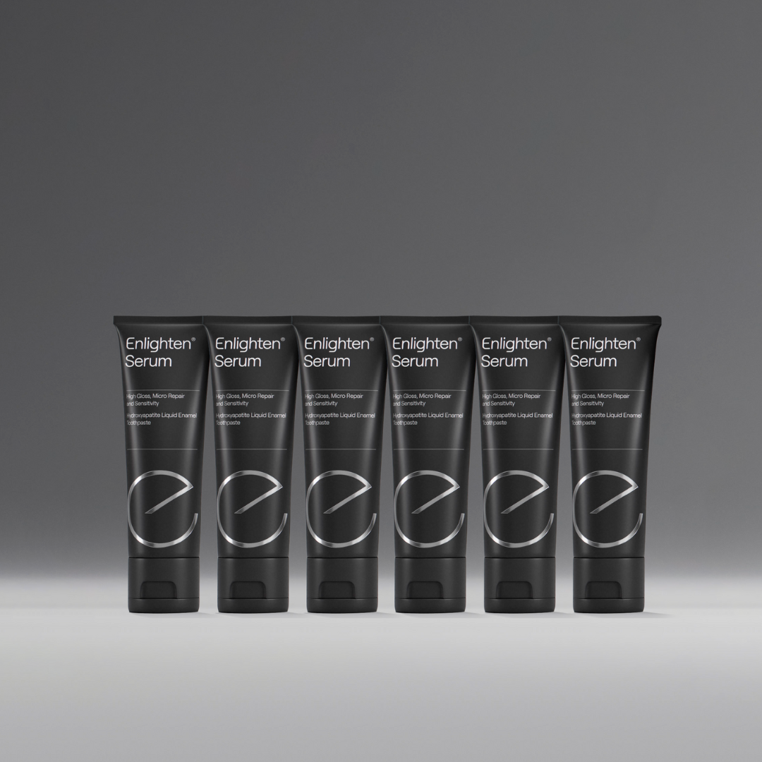 A row of six Enlighten Serum tubes displayed uniformly against a neutral grey background. The sleek black tubes feature the Enlighten logo and branding, highlighting the product's premium and professional appearance.