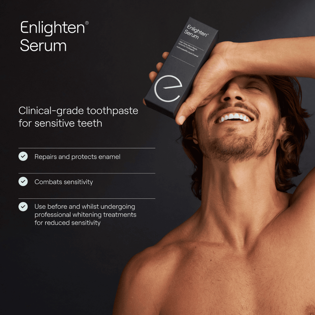 A promotional image for "Enlighten Serum," featuring a smiling man with healthy teeth holding the product's sleek black box. The tagline reads, "Clinical-grade toothpaste for sensitive teeth," accompanied by benefits listed with checkmarks: "Repairs and protects enamel," "Combats sensitivity," and "Use before and whilst undergoing professional whitening treatments for reduced sensitivity." The man’s relaxed, joyful expression and bare shoulders convey confidence and comfort, set against a dark, background.