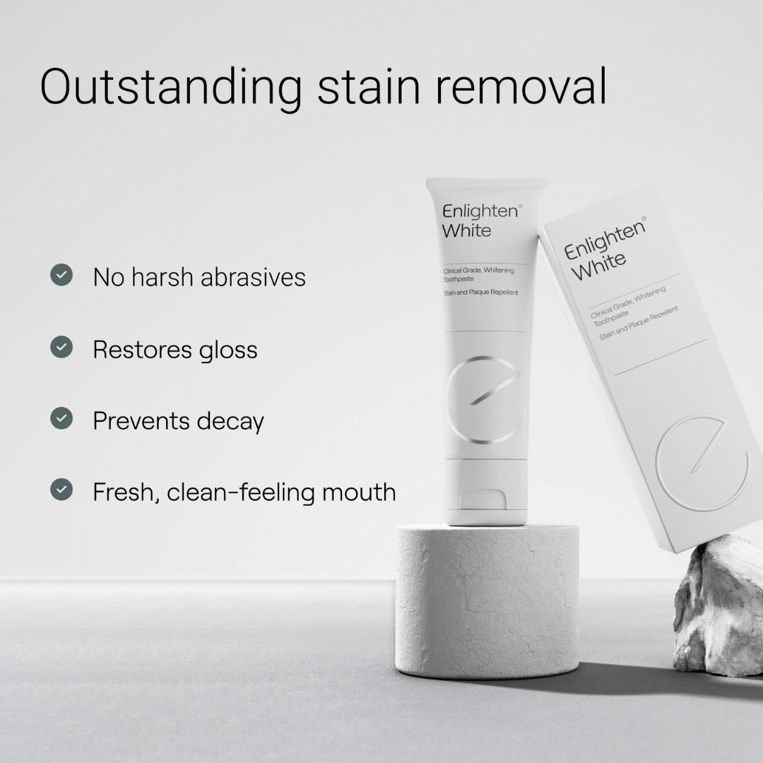 A promotional image for Enlighten White toothpaste, featuring the tagline "Outstanding stain removal." The white tube and box are displayed on a textured stone pedestal against a clean, minimalist background. Key benefits are listed: "No harsh abrasives, restores gloss, prevents decay, fresh, clean-feeling mouth." The professional design highlights the product's premium quality and gentle yet effective whitening properties.