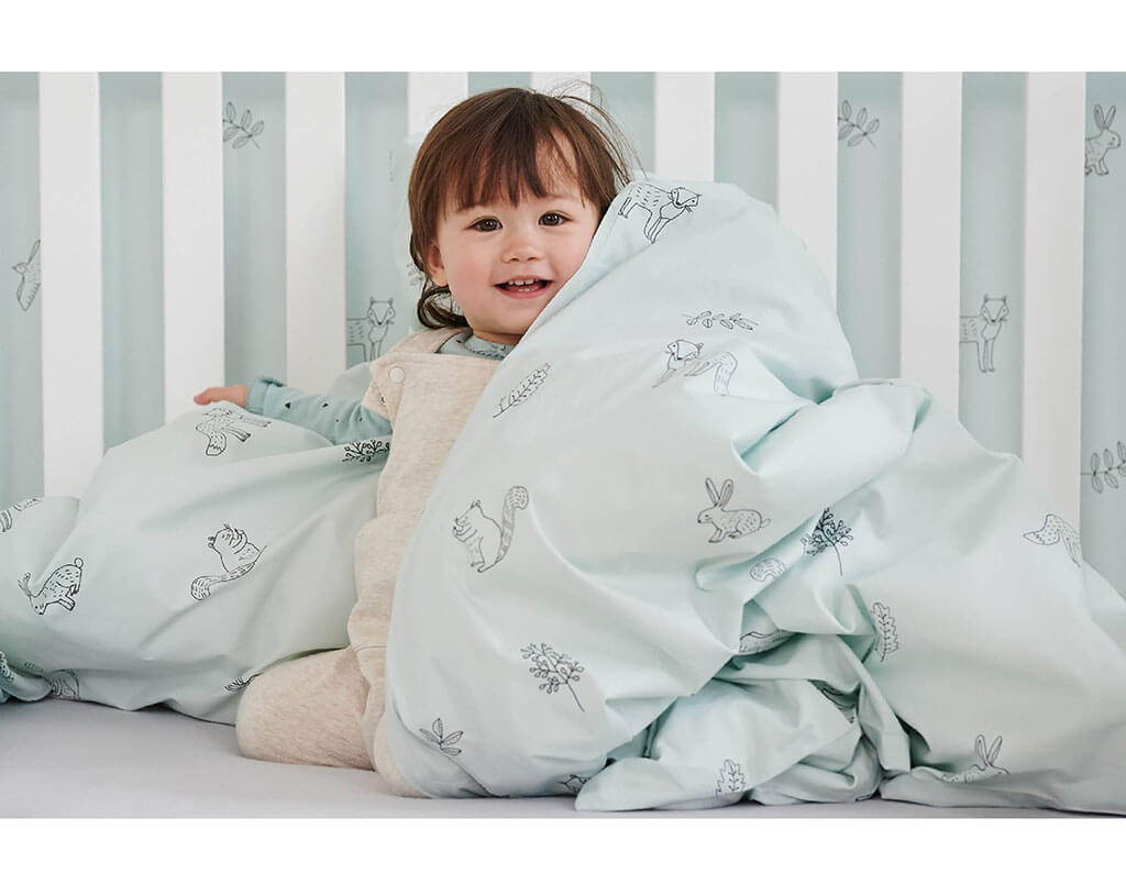 Toddler wrapped in children's woodland bedding