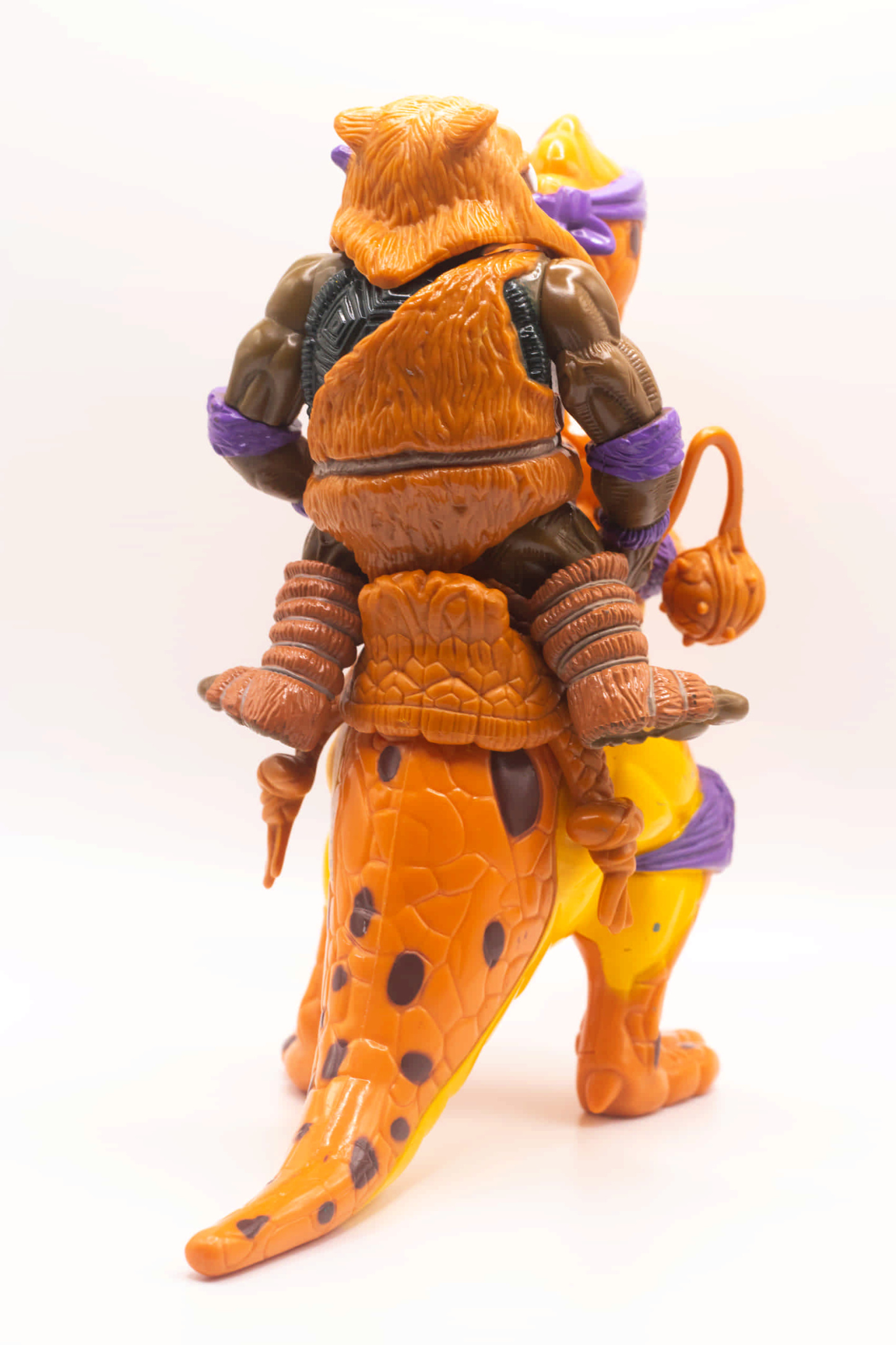 Rear view of vintage Cave-Turtle Don action figure holding Mesozoic Mace, riding on Trippy Tyrannosaurus