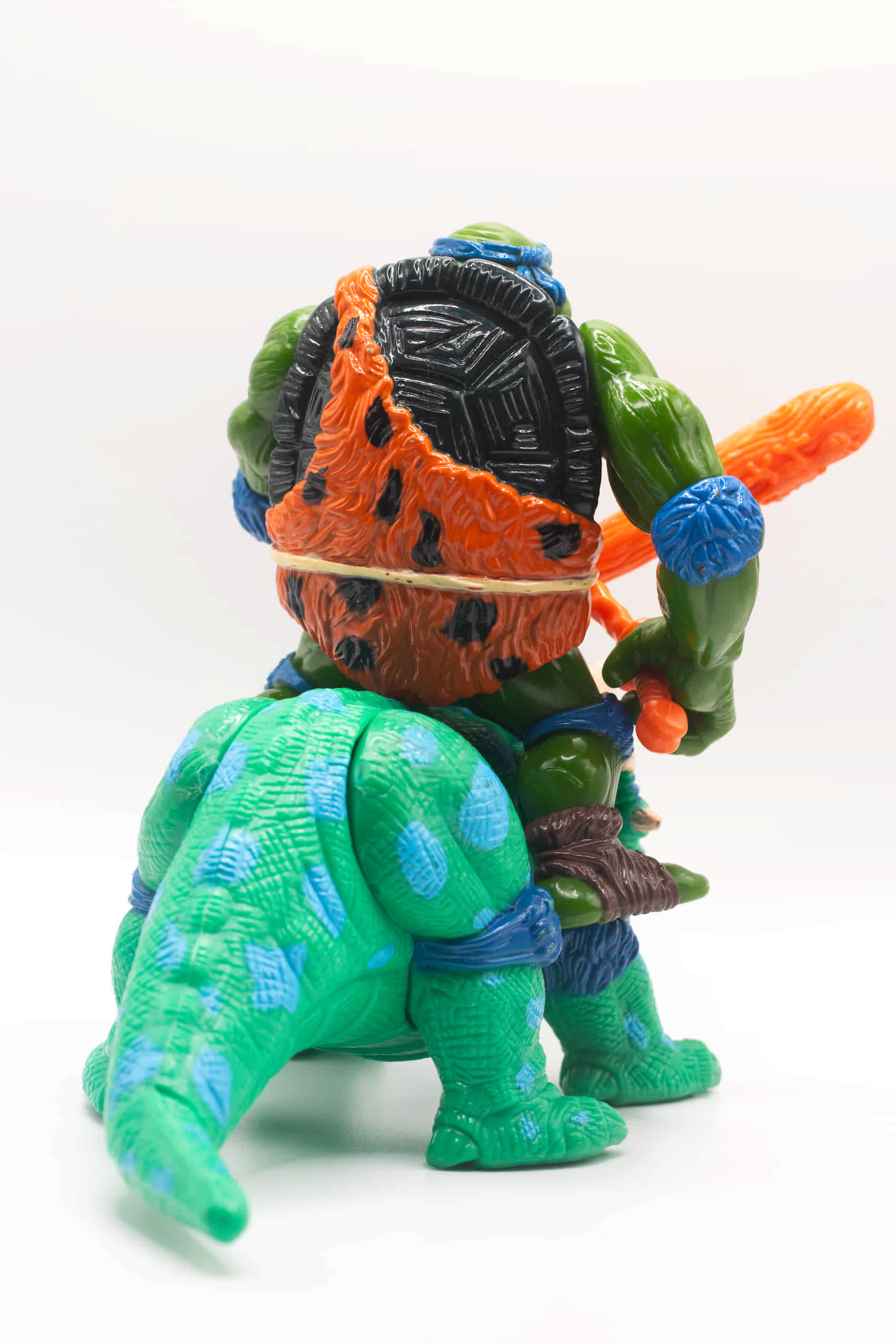 Rear view of vintage Cave-Turtle Leo action figure holding katana and club, riding Dingy Dino