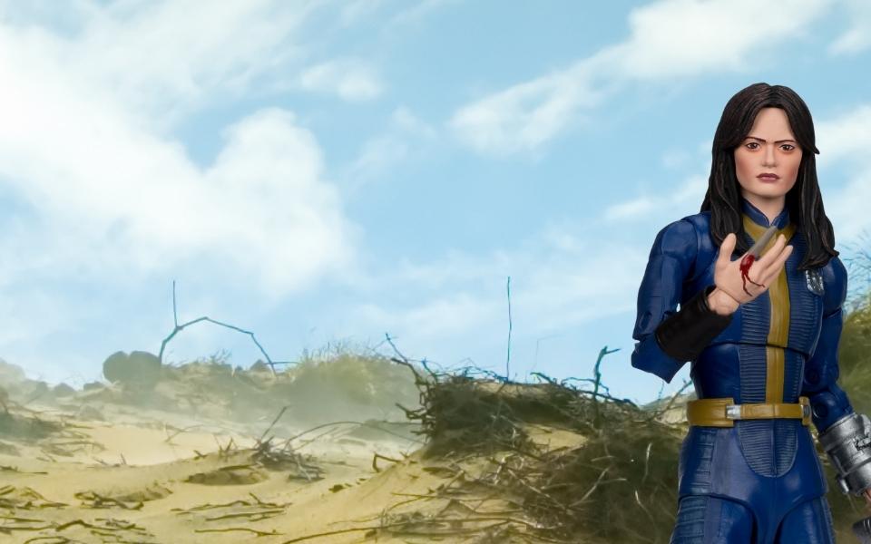 {"default":"Wasteland scene with Lucy Fallout action figure in a blue Vault 33 suit with bloodied finger"}
