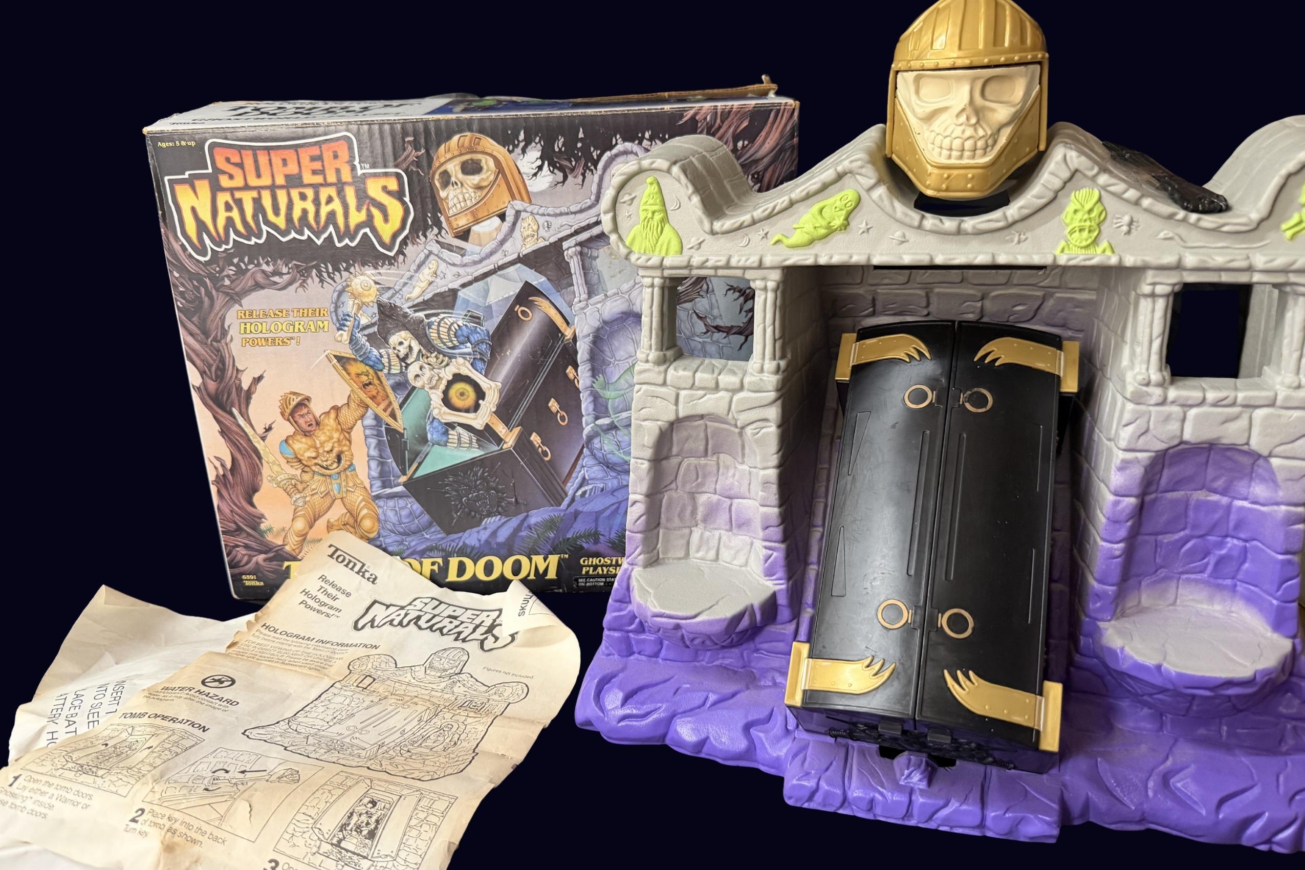 Vintage Super Naturals Tomb of Doom playset box beside assembled grey and purple tomb with gold skull head and black coffin door, instruction sheet in front