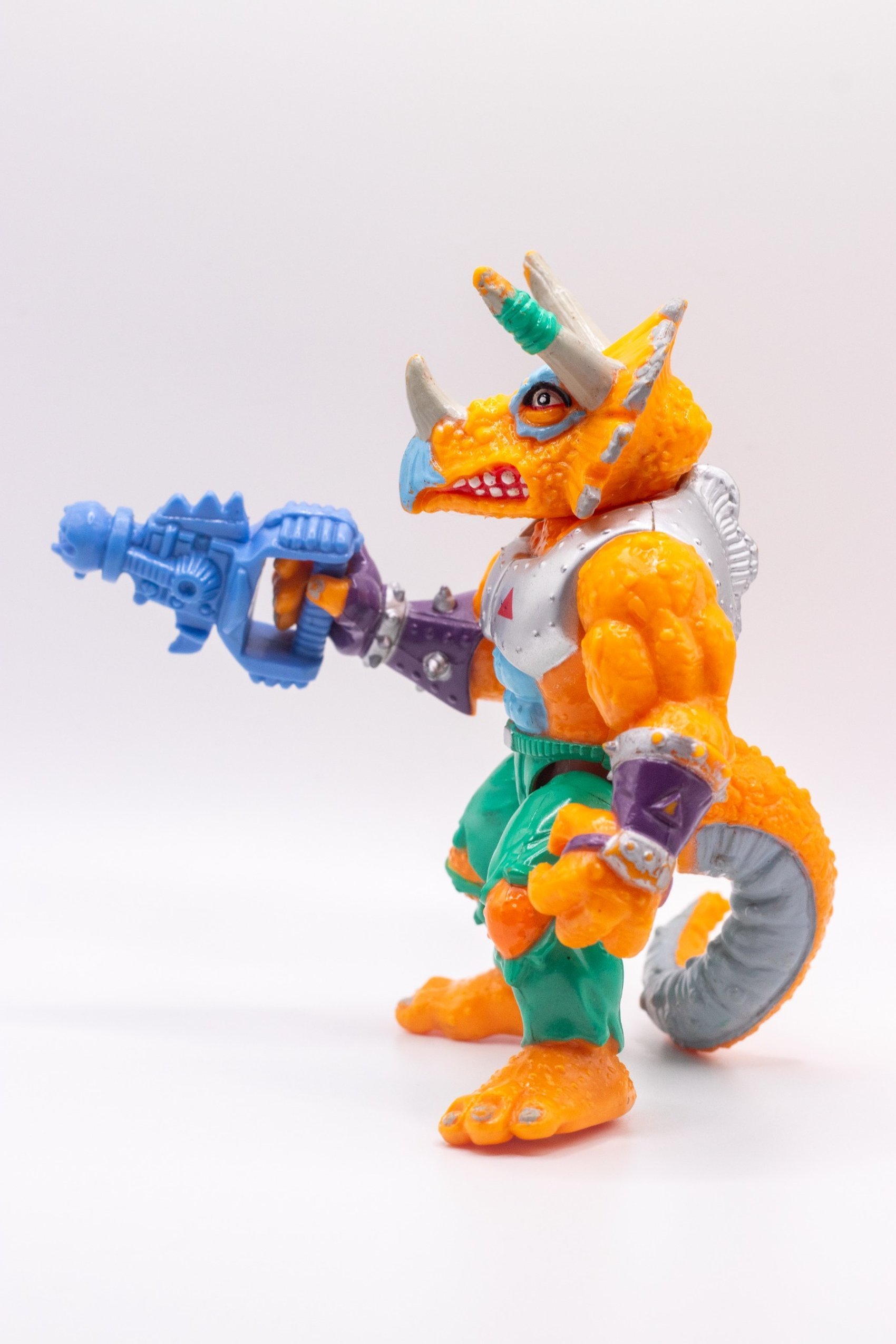 Left side view of Triceraton action figure aiming Laser Phaser with curled tail in frame