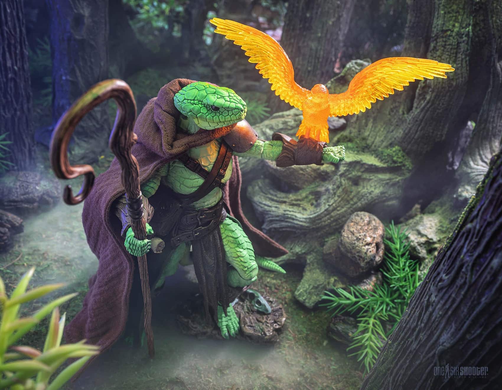Dynamic forest shot of Vernaliss Ardenscale action figure in brown cloak holding staff and glowing orange bird companion