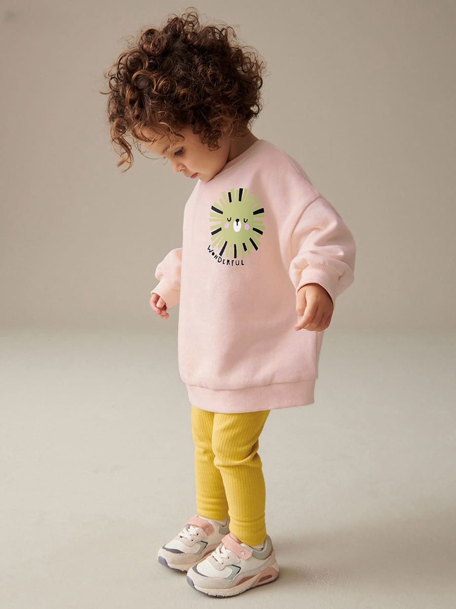 Girls pink smiley face print cotton sweatshirt and pants set, relaxed fit, playing outdoors.