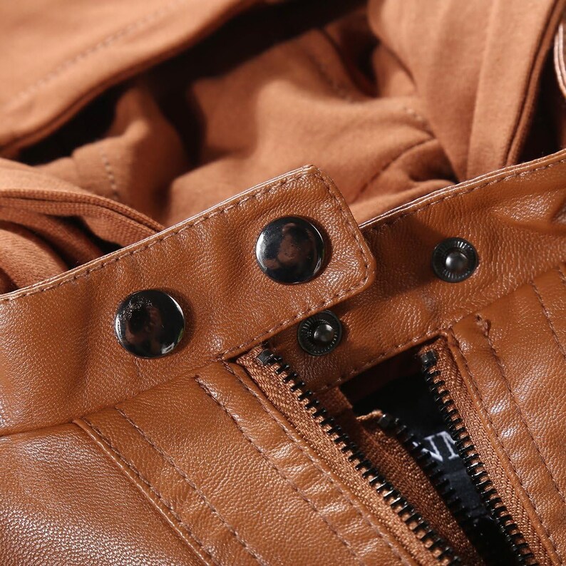 May include: Close-up of a brown leather jacket zipper and button closure. The zipper is partially open and the buttons are metal with a silver finish.