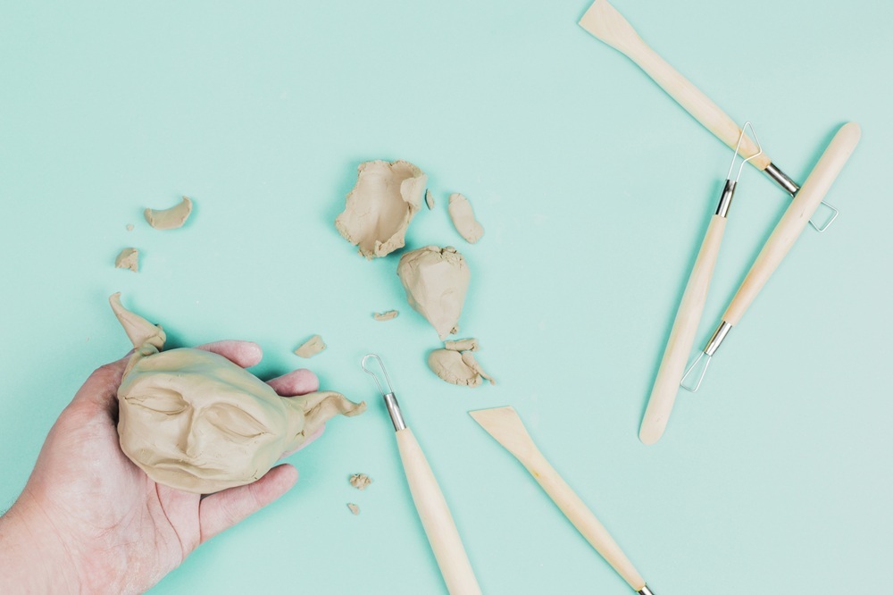 Hands shaping a small clay sculpture with a sculpting tool