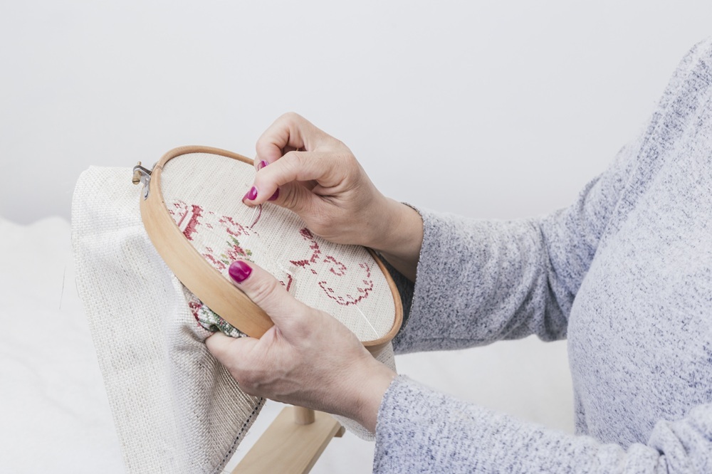 Hands stitching a floral pattern in an embroidery hoop