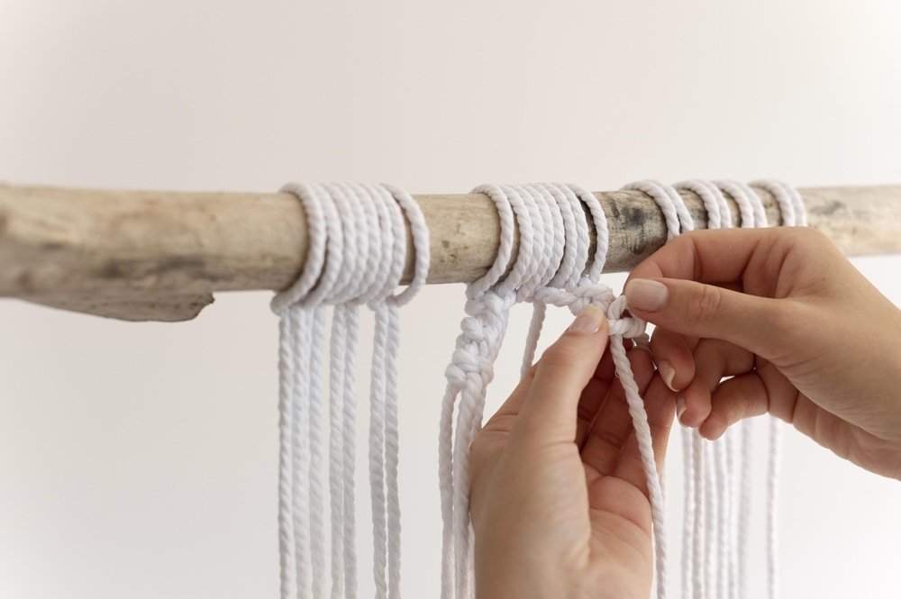 Hands knotting white cords to make a macrame wall hanging