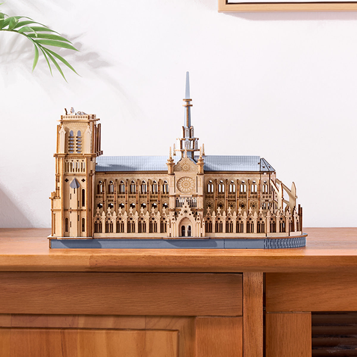 Rowood Paris Cathedral TG511 wooden puzzle side-angle view placed on a wooden cabinet with warm ambient light, showing the rear towers and flying buttresses