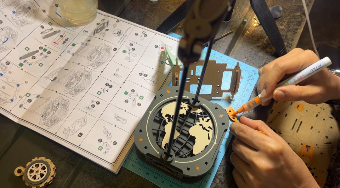 Aiffah coloring an orange Road Tripper piece beside the instructions and partially assembled model