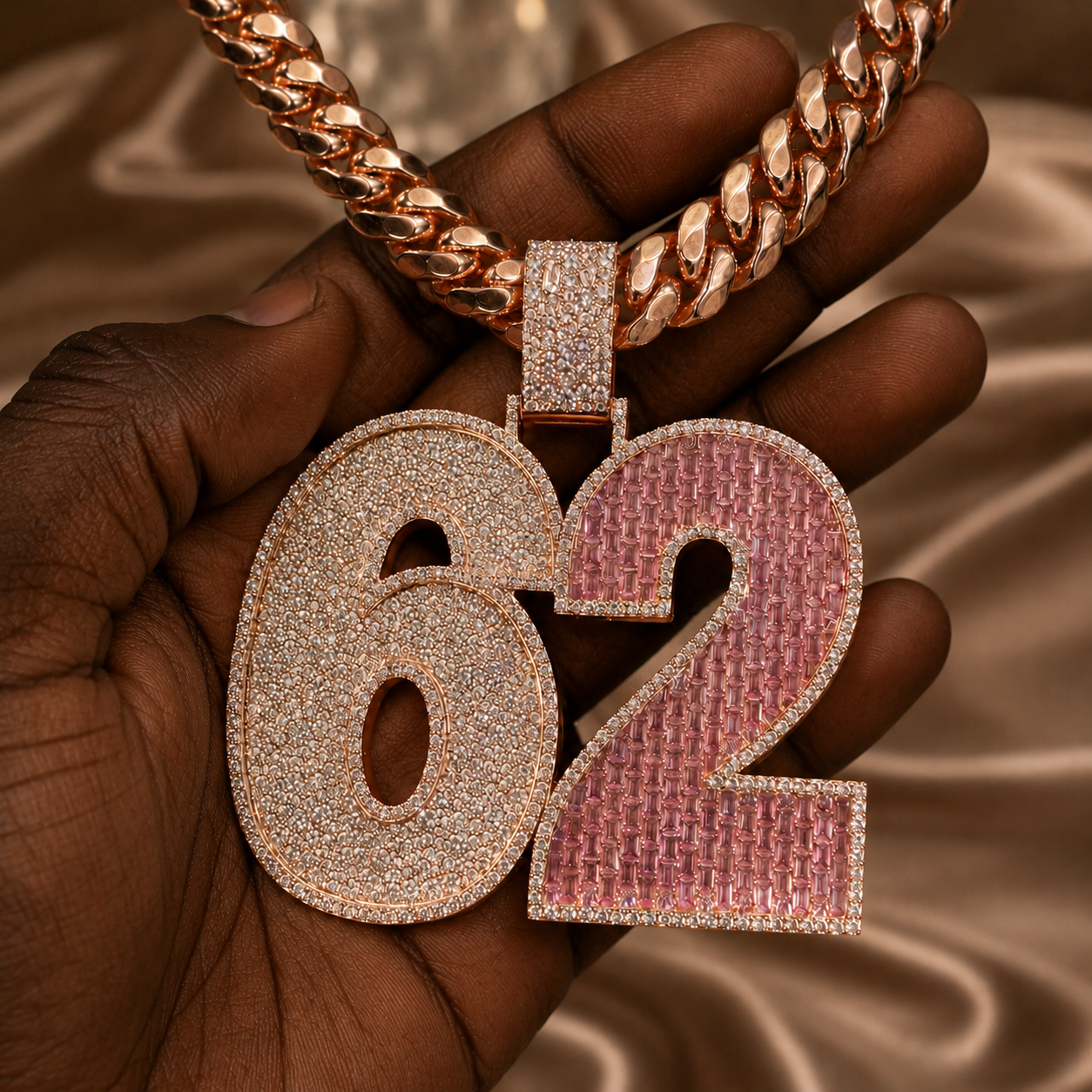 Iced out 62 pendant displayed in hand with sparkling clear stones and pink gemstone detail.