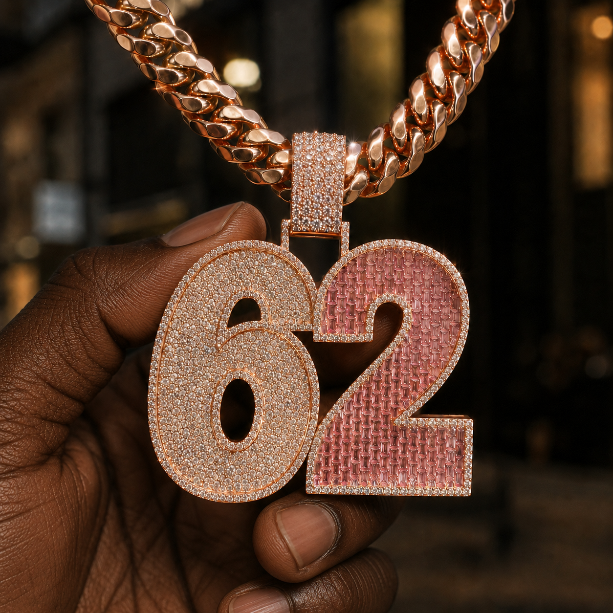 Iced out 62 pendant displayed in hand with sparkling clear stones and pink gemstone detail.
