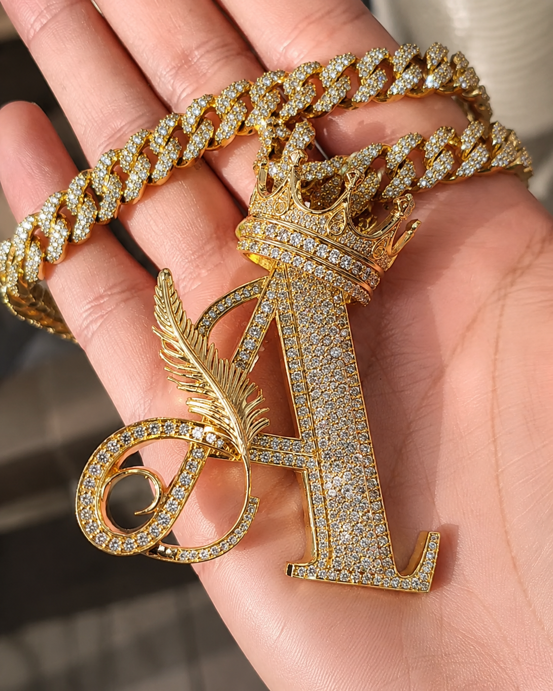 Gold iced-out Letter A crown pendant with Cuban link chain held in hand