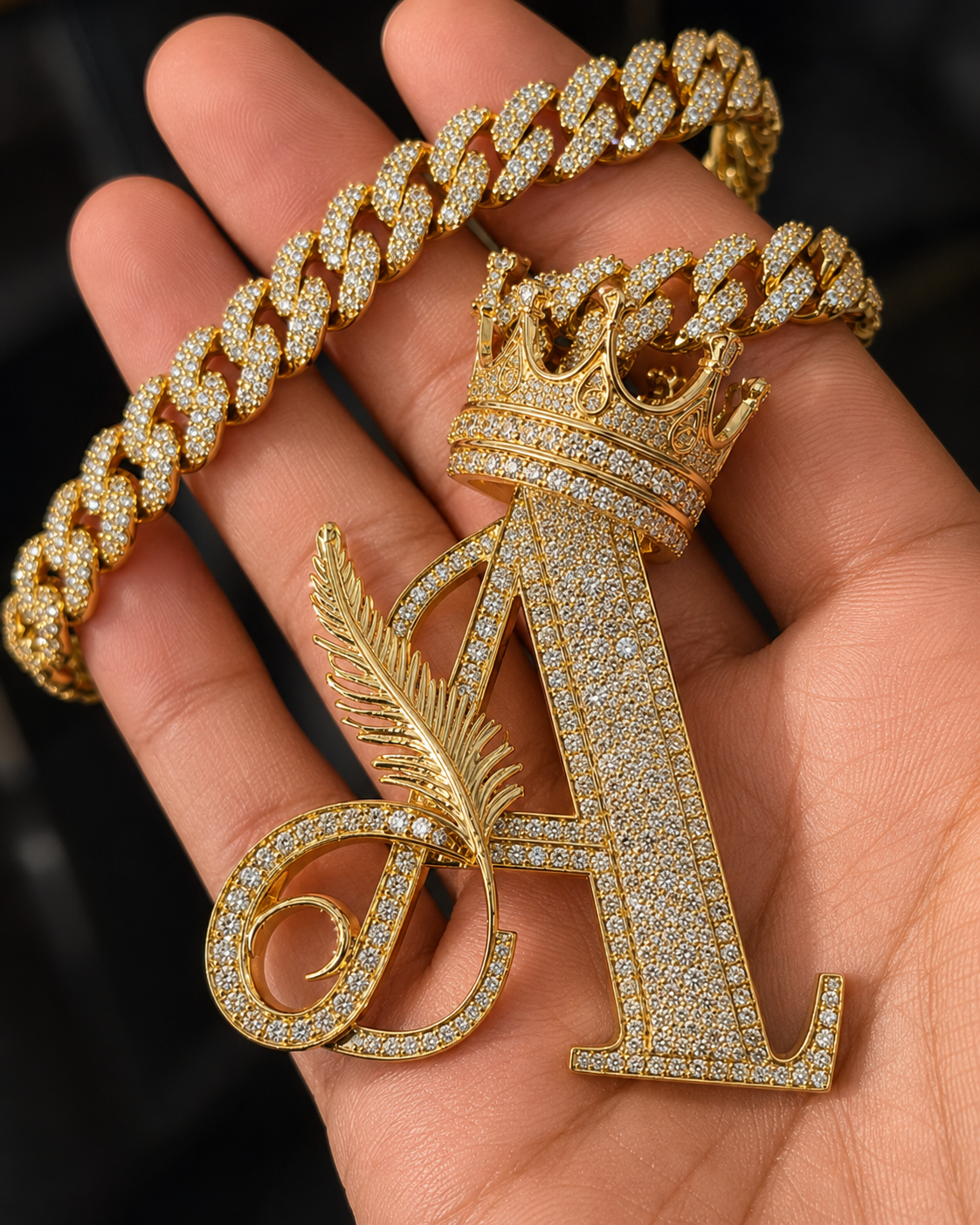 Gold iced-out Letter A crown pendant with Cuban link chain held in hand