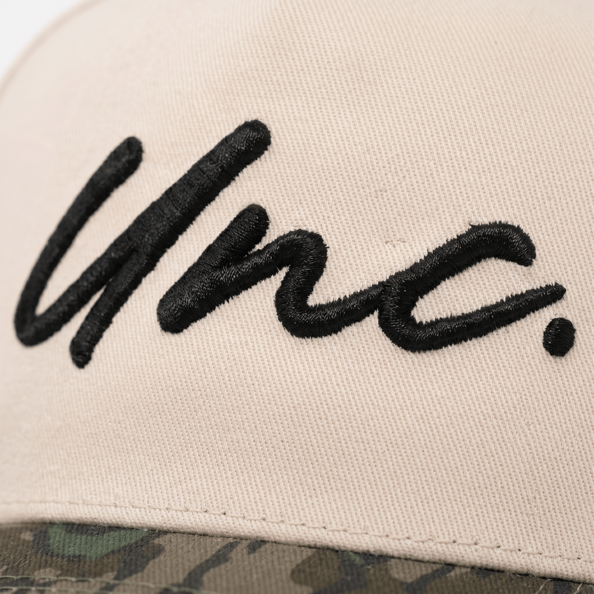 Close-up of black Unc embroidery on cream cap with camo brim