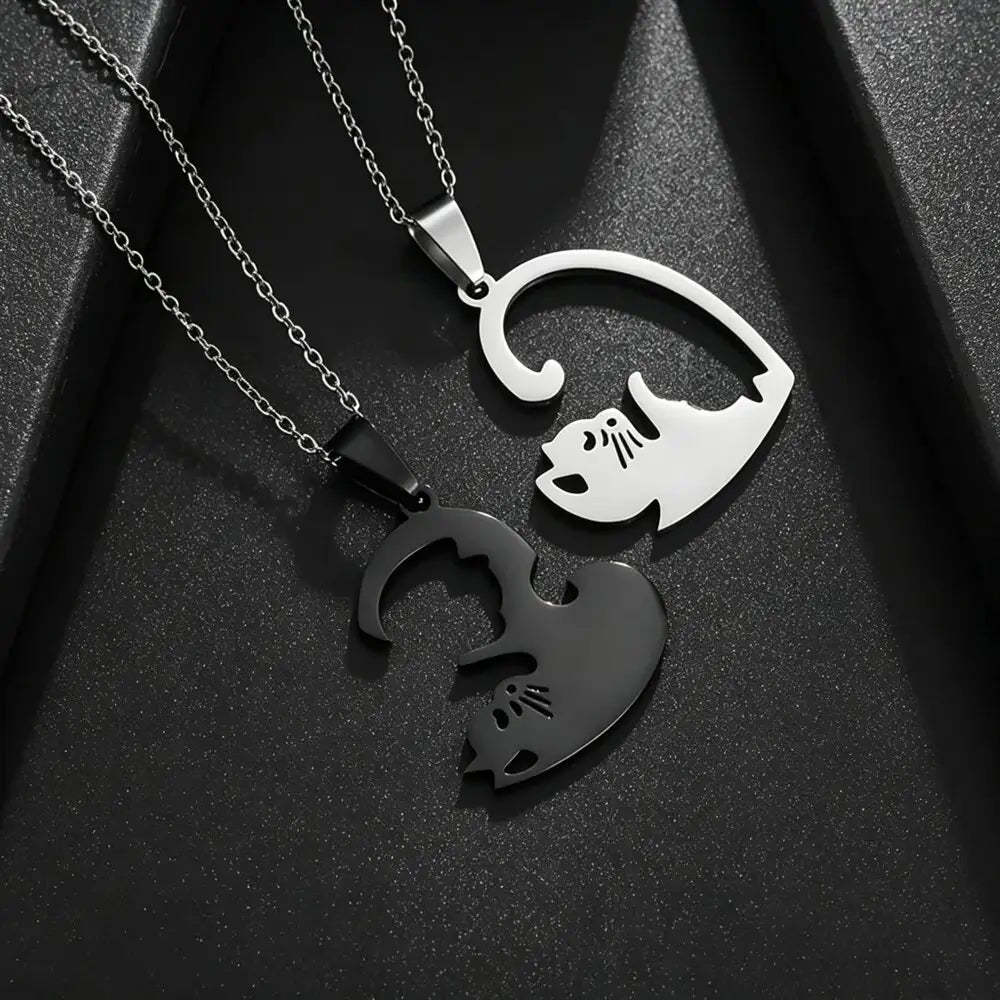 Two interlocking cat-shaped pendant necklaces on chains, one polished silver and one matte black, displayed on a textured black background.