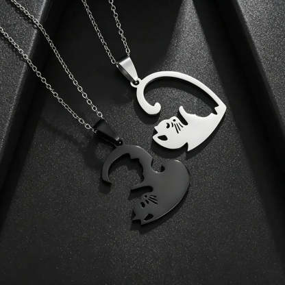 Two interlocking cat-shaped pendant necklaces on chains, one polished silver and one matte black, displayed on a textured black background.