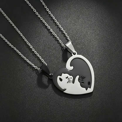Two silver heart-shaped pendant necklaces on matching chains, designed to fit together into one heart. One pendant is polished silver with a black cat silhouette, and the other is black with a silver cat silhouette, set against a dark textured background.