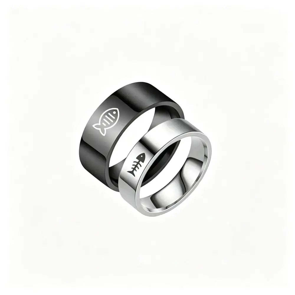 Two interlocking stainless steel rings on a plain white background. The top ring is black with a white fish symbol, and the bottom ring is silver with a black fish skeleton symbol.