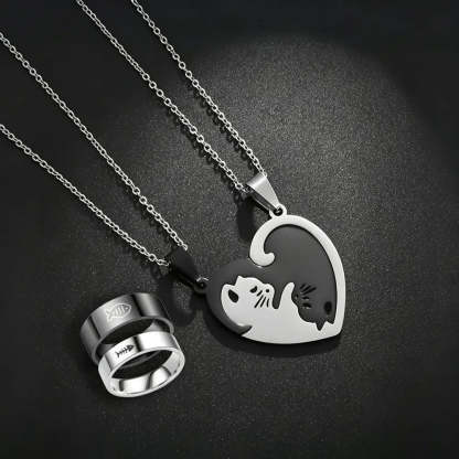 Two silver-toned necklaces and matching rings displayed on a dark textured background. One necklace has a heart-shaped pendant split into white and black halves forming a cat and dog silhouette.