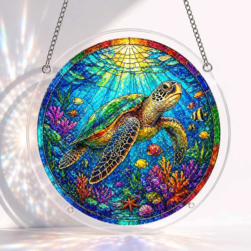 A round acrylic suncatcher of a green sea turtle swimming among colorful coral reef fish and sunlit ocean water